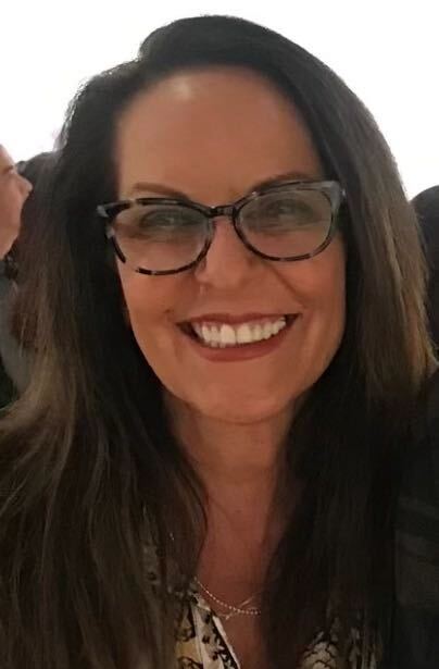 A woman with long dark hair and glasses smiling at the camera.