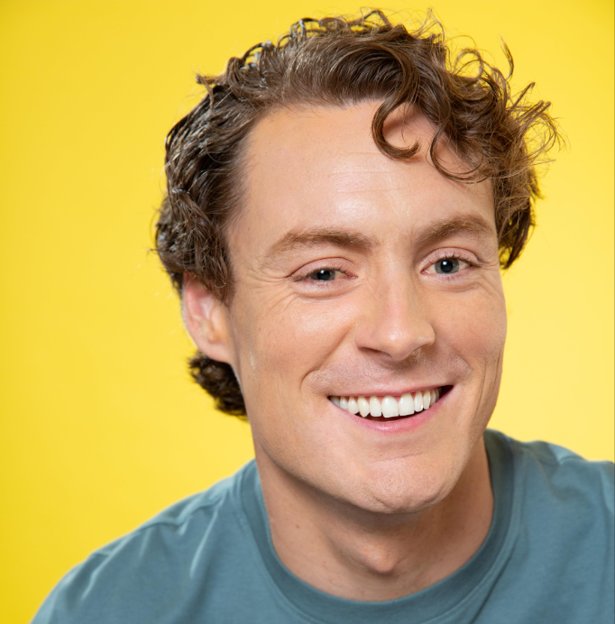 A person with curly brown hair smiles against a yellow background.