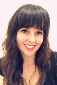 Woman with long wavy brown hair and bangs, wearing a black top, smiling at the camera against a light background.