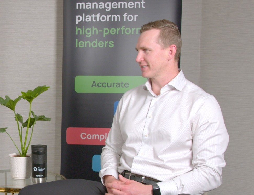 A man in a white shirt sits beside a plant and a branded cup, with a banner in the background reading "management platform for high-performance lenders.