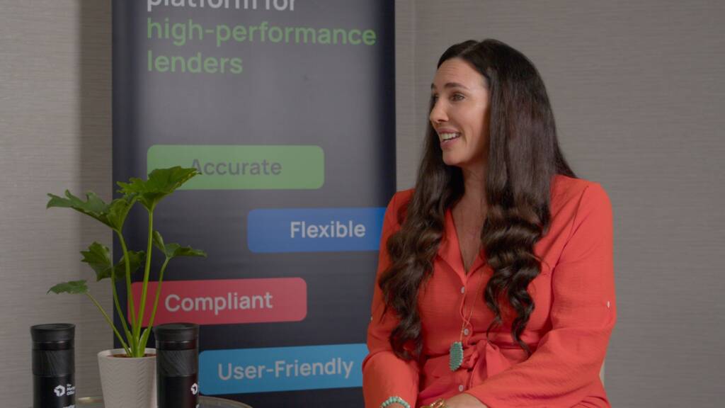 A woman with long brown hair wearing an orange blouse sits and smiles near a plant and a banner displaying business keywords.