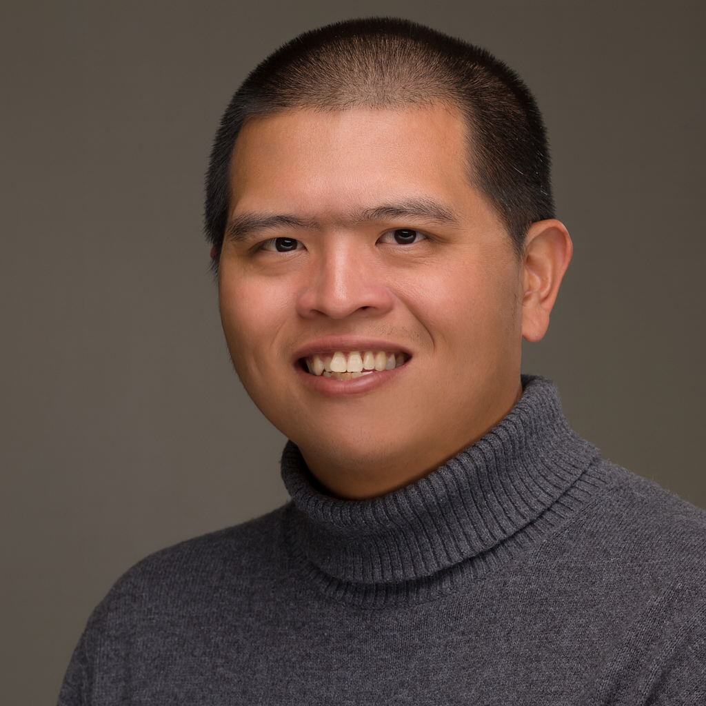 A person with short black hair, wearing a gray turtleneck sweater, smiles at the camera against a plain background.
