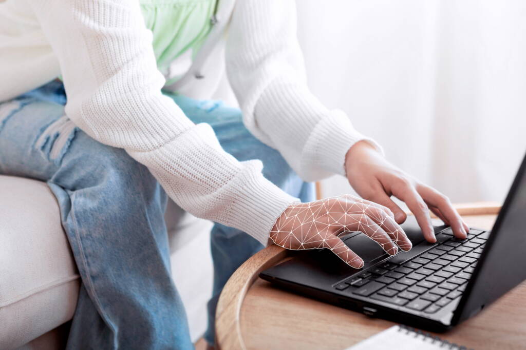 Child's hands typing on a laptop keyboard while wearing a white sweater.