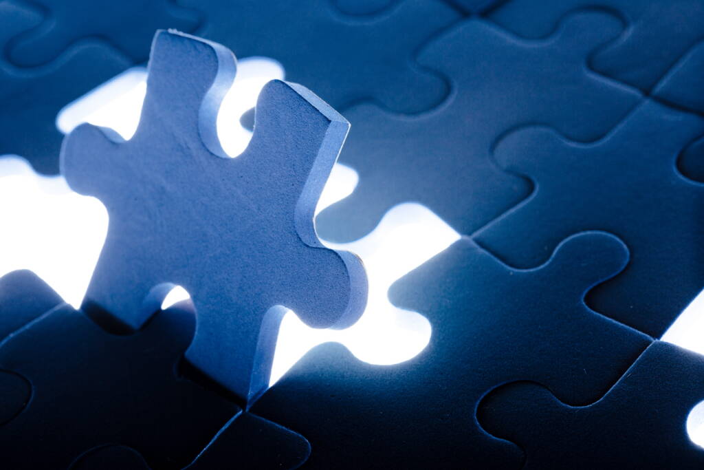 A blue puzzle piece stands upright among other puzzle pieces, with bright white light glowing.